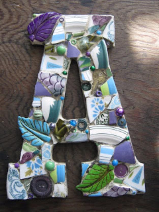 Custom mosaic letter A covered in blue, green and purple china pieces, carved stone leaves and glass buttons, on dark wood