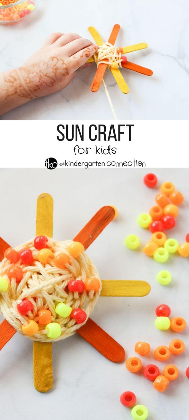 Woven yarn and pony bead sun on crossed orange popsicle sticks, shown below a photo of a child's hand holding the sticks