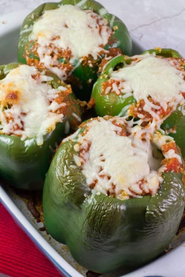 Quinoa and kale stuffed green peppers topped with melted mozzarella standing upright in a baking dish