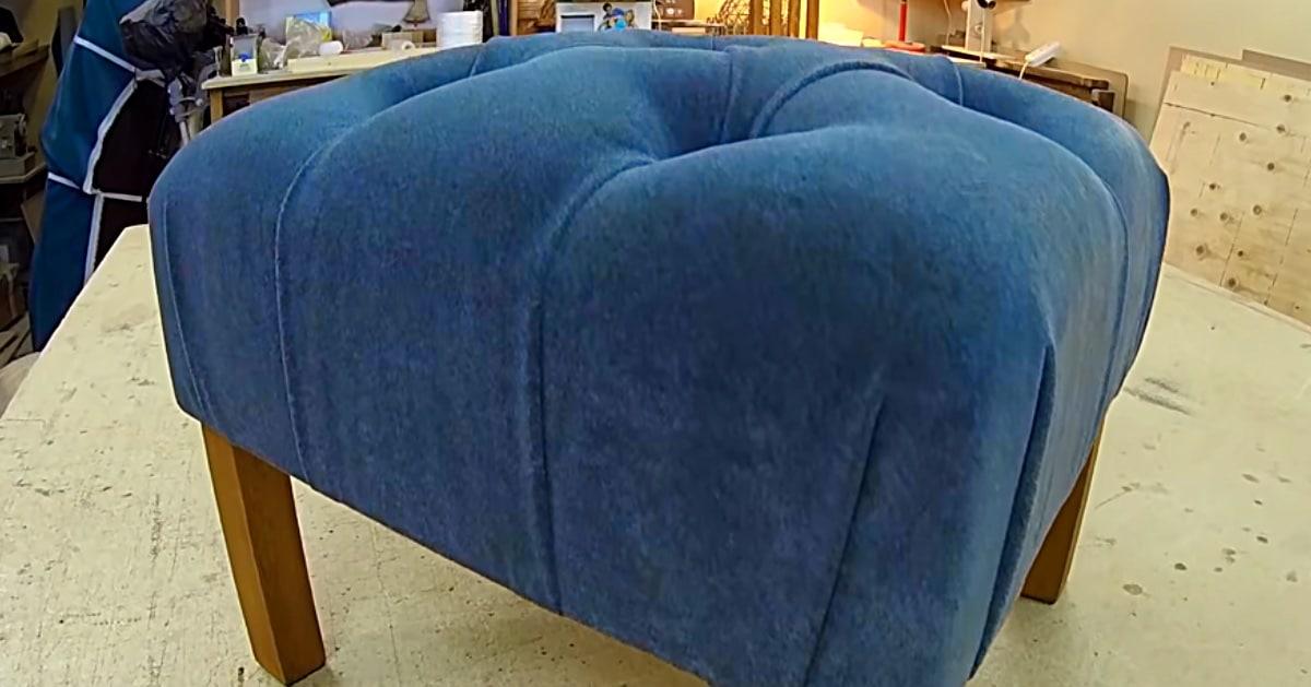 Deep blue velvet tufted pouf ottoman on four short wooden legs, standing on a workbench in a workshop
