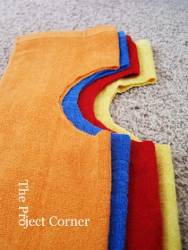 DIY towel bibs in orange, blue, red and yellow, fanned out on carpet to show the cut neck opening on each one