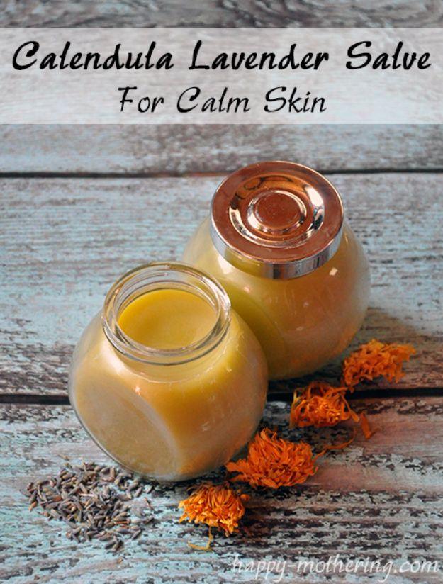 Two small glass jars of yellow calendula lavender salve on blue wood with orange petals and lavender