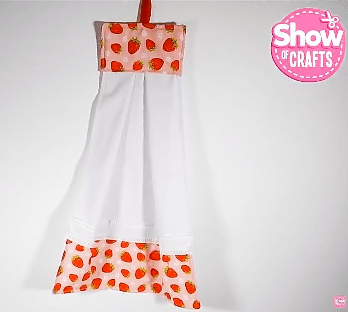A towel dress in floral and gingham fabric with a ribbon tie at the waist, hanging from an oven door handle