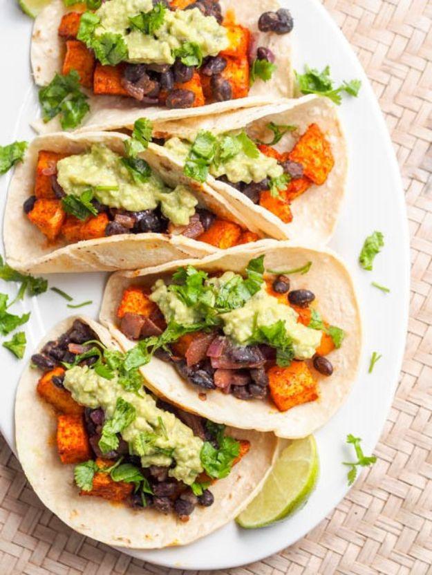 Vegan butternut squash tacos on a plate with black beans, avocado crema dollops, cilantro and a lime wedge