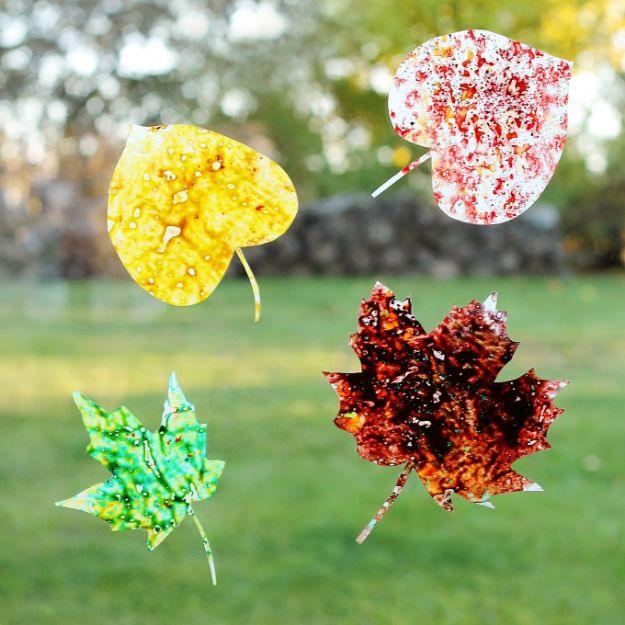 Four melted crayon leaf suncatchers in yellow, speckled red, green and dark red hanging outdoors against grass
