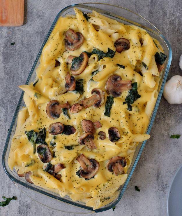 Vegan pasta bake in a glass dish with penne, sliced mushrooms and spinach under a creamy golden cheese sauce