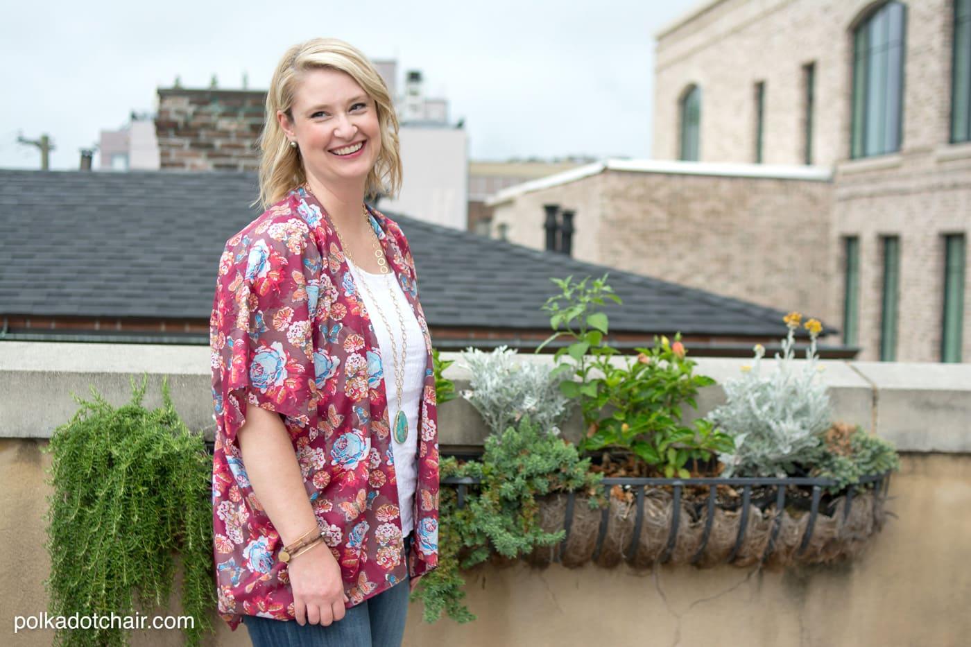 Woman in a red and white floral kimono top over a white tank top, standing on a rooftop beside planters