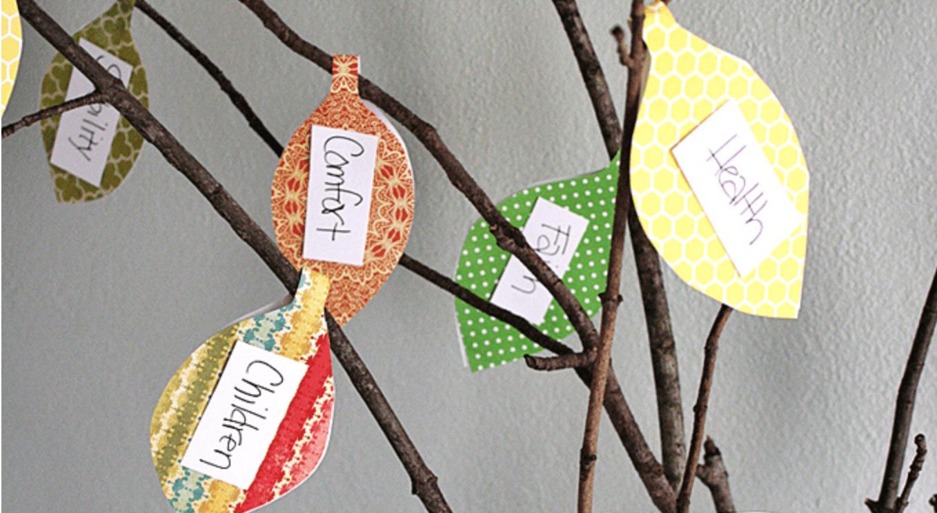 Family thankful tree made from branches in a mason jar hung with folded scrapbook paper leaves and cardstock notes