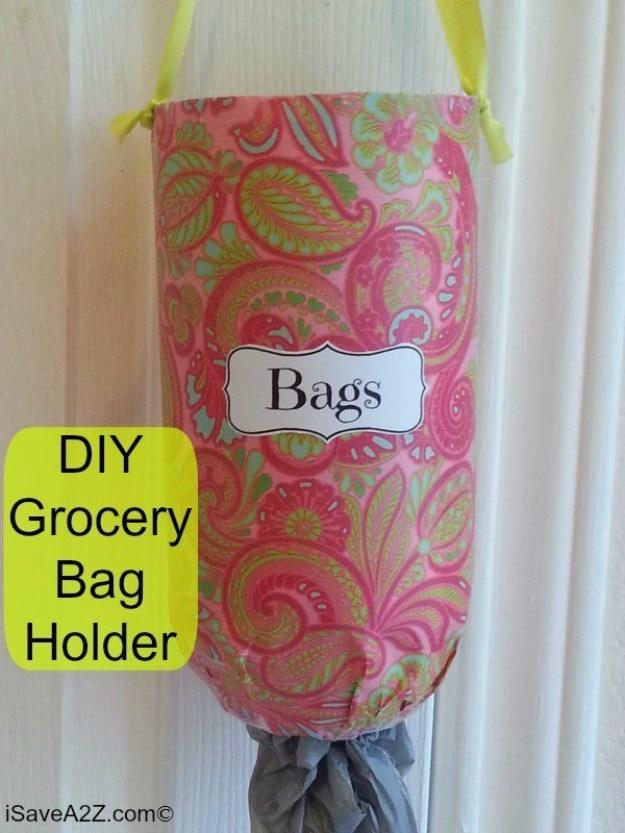 Plastic grocery bag holder made from a cut bottle wrapped in decorative paper, hanging by a ribbon and dispensing bags