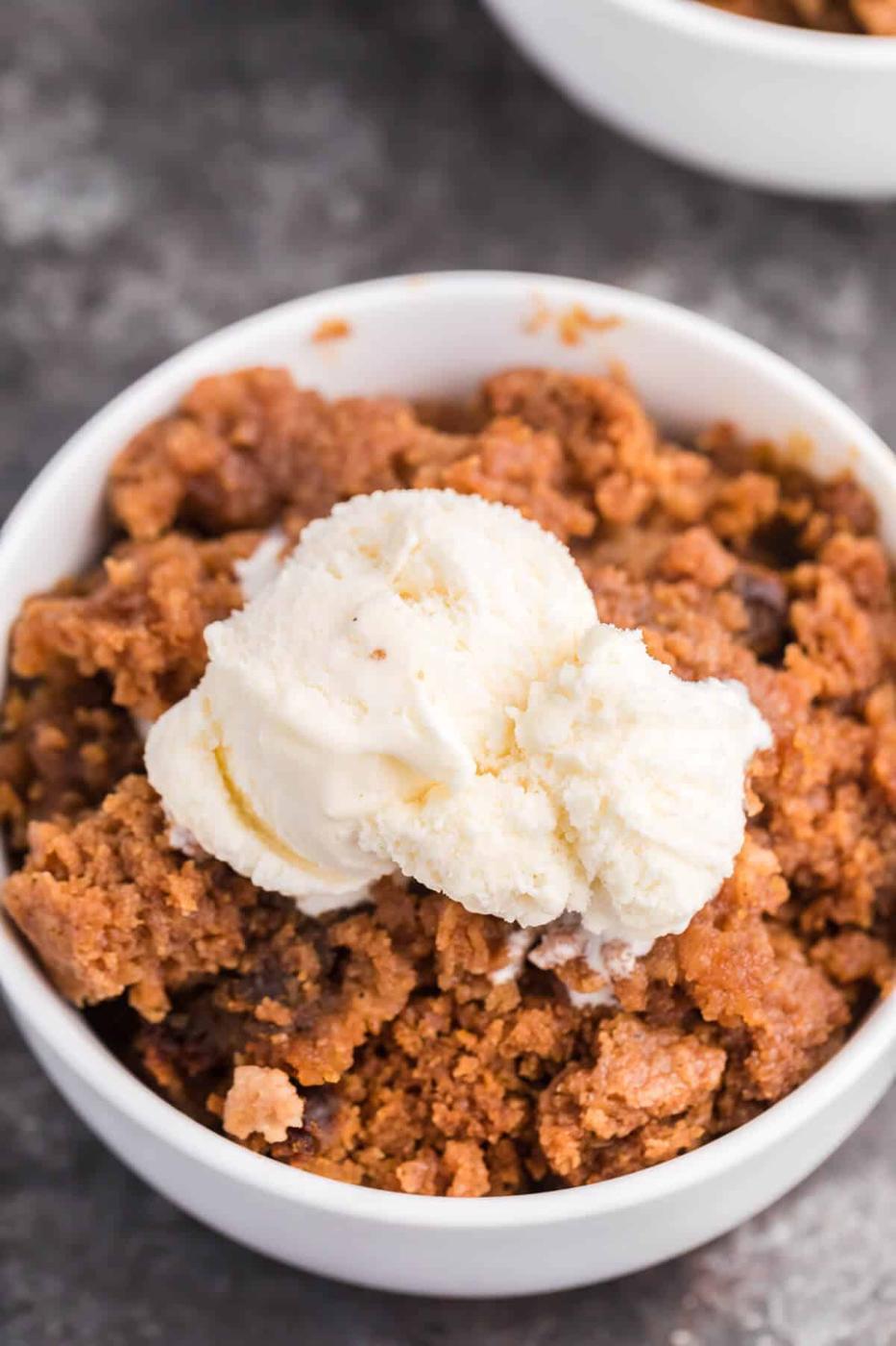 Pumpkin dump cake in a white bowl topped with vanilla ice cream as a finished slow cooker holiday dessert
