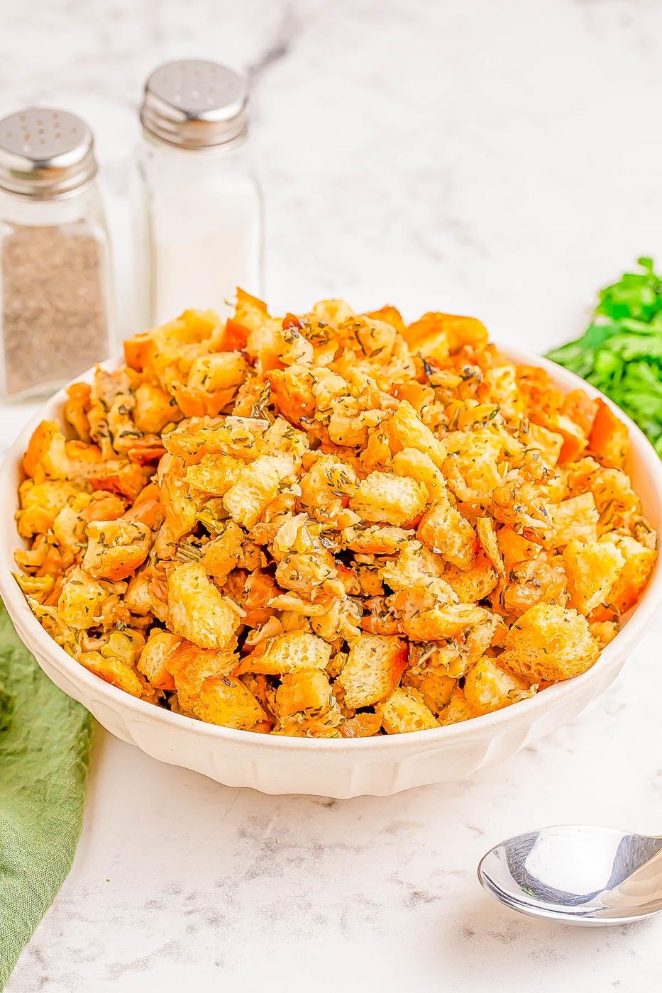 Herb stuffing in a white bowl with parsley, serving spoon, salt and pepper shakers and a green cloth