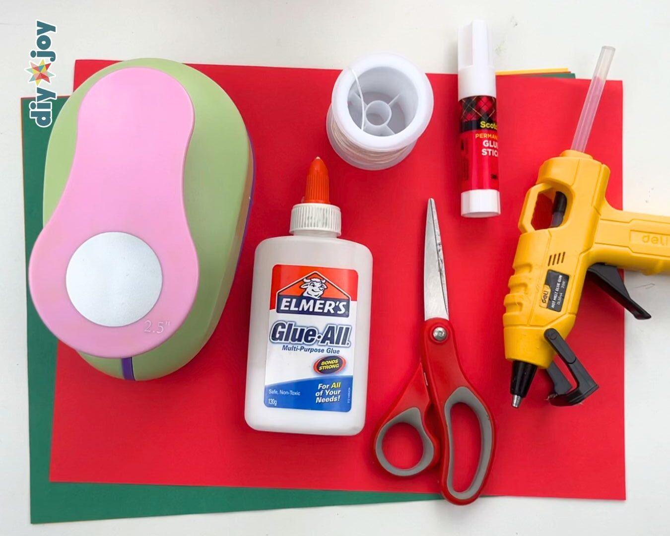 DIY Projects - craft supplies for paper ornaments laid out on cardstock, including a round paper punch, white glue, string, a glue stick, scissors, and a hot glue gun