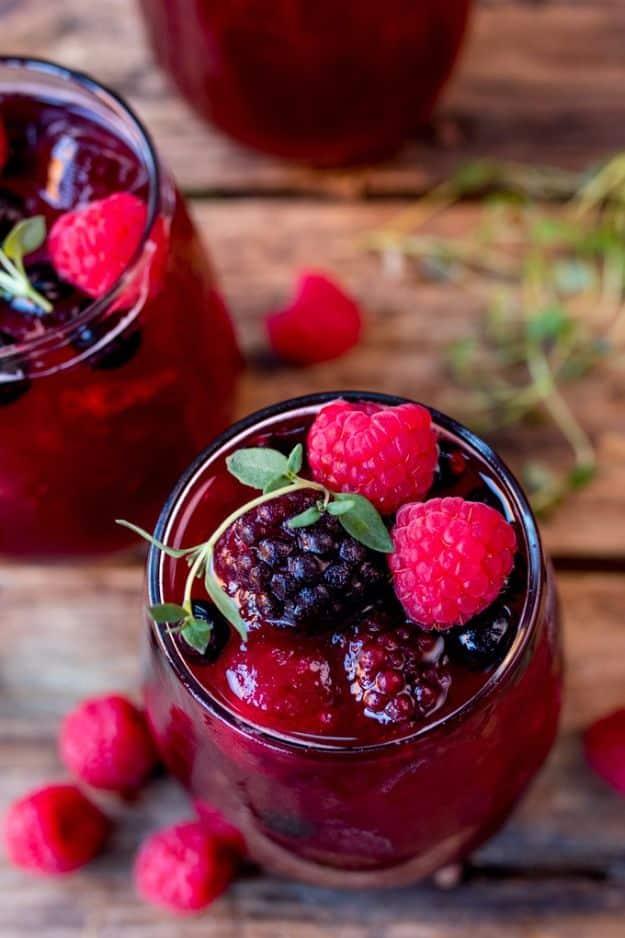 A jug and glass of deep red New Year's Eve rum berry cocktail filled with frozen berries and fresh raspberries