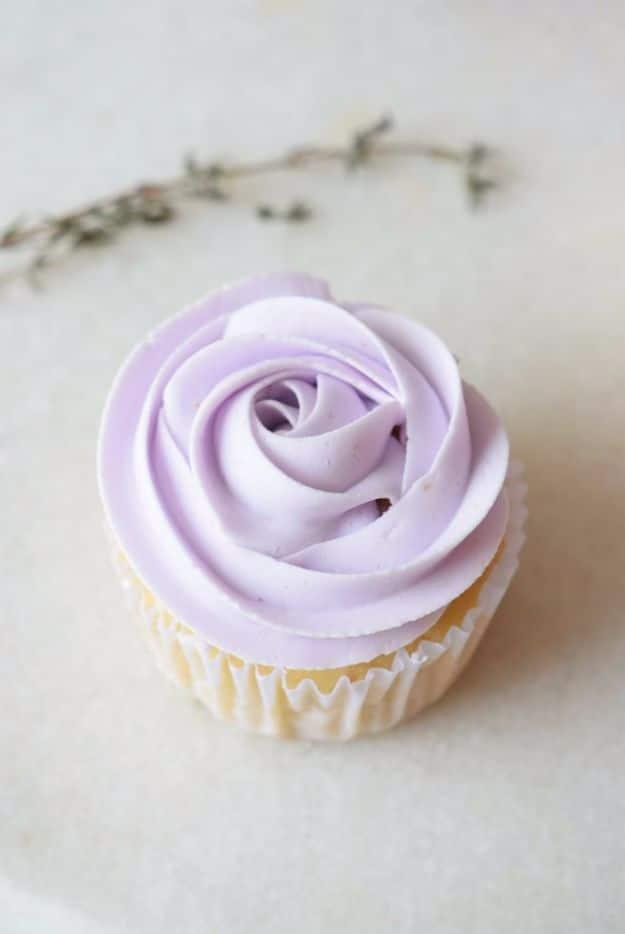 Single lavender cupcake in a white paper case topped with a pale purple frosting rose on white marble