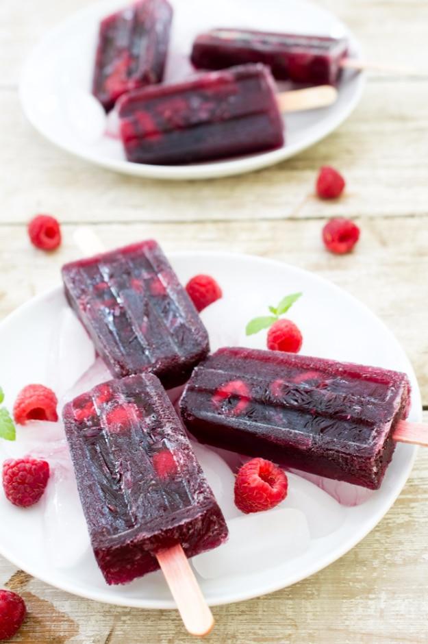 4 ingredient raspberry sangria popsicles on white plates with fresh raspberries, a frozen summer dessert idea
