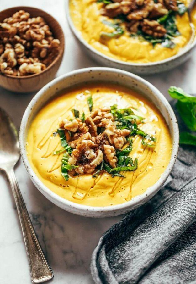 Golden turmeric vegetable soup in a speckled white bowl, topped with whole walnut halves and shredded basil