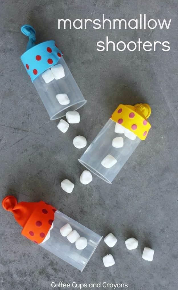 Three clear cake pop tube shooters with blue, yellow and orange polka dot balloon ends, spilling mini marshmallows