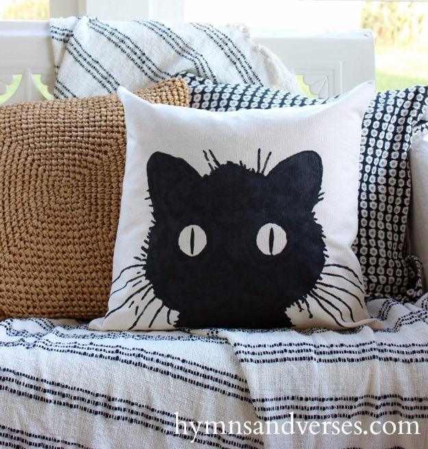 No sew black cat pillow cover, a white canvas cushion painted with a large black cat face among woven throw pillows