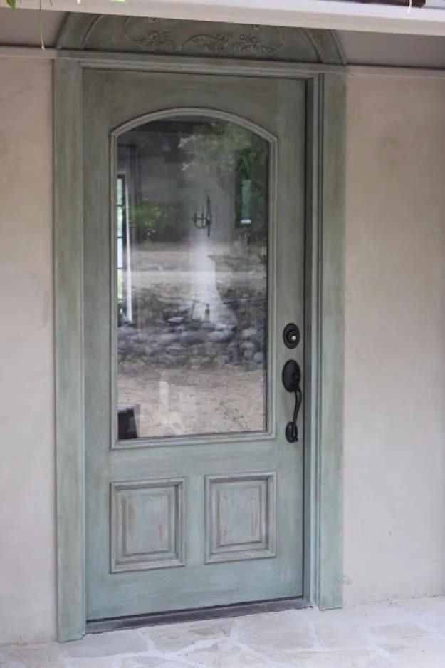 Arched glass front door painted a soft distressed turquoise grey, set into matching painted trim and stonework