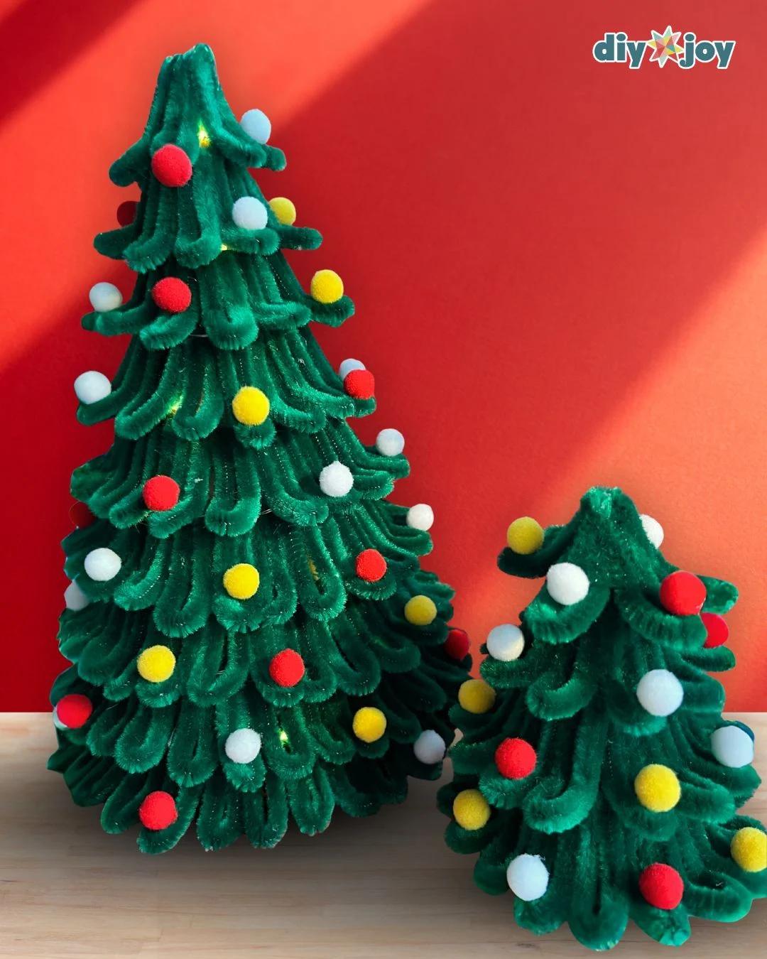 Christmas Decor Ideas - a tall and a medium finished pipe cleaner tree standing side by side on wood against a red wall in warm light