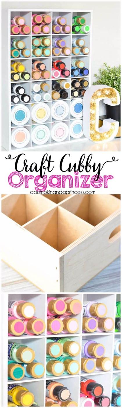 White cubby organizer in a wooden crate holding craft paint bottles on their sides by color, gold marquee letter beside