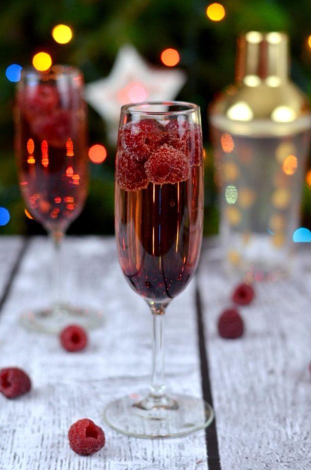 Champagne flutes of raspberry Chambord cocktail with fresh raspberries rising through the bubbles, party lights