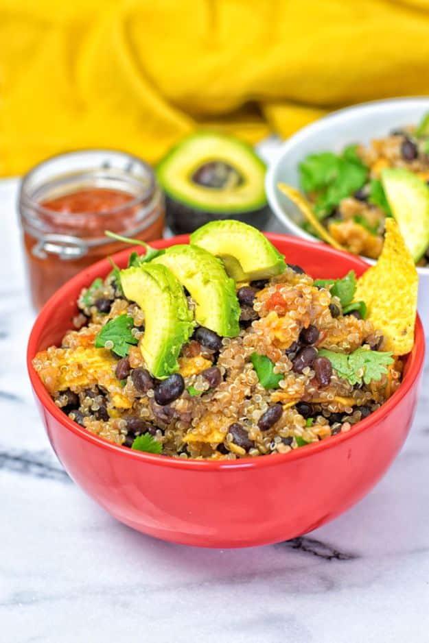 Quinoa taco salad in a red bowl with black beans, sliced avocado and a tortilla chip, salsa alongside