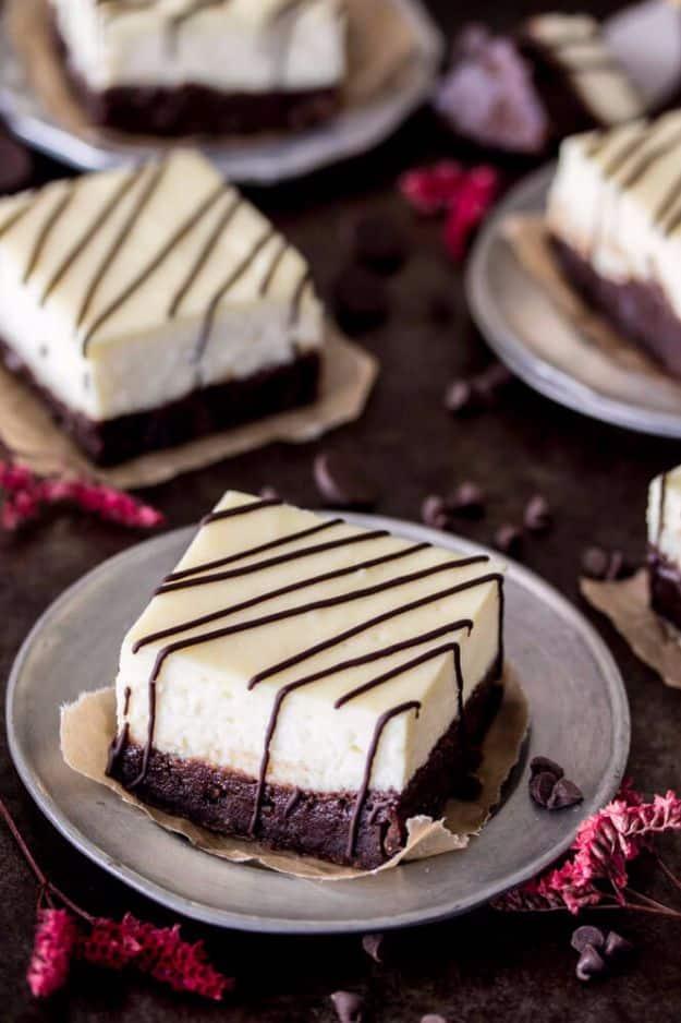Cheesecake brownie bars on a grey plate, white cheesecake over dark brownie with straight diagonal chocolate lines