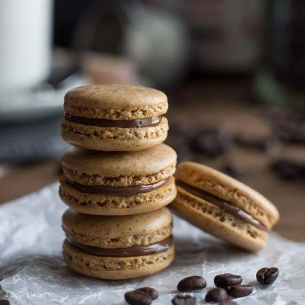 Coffee macarons stacked in a tower with dark Nutella filling showing at the edges, coffee beans on parchment