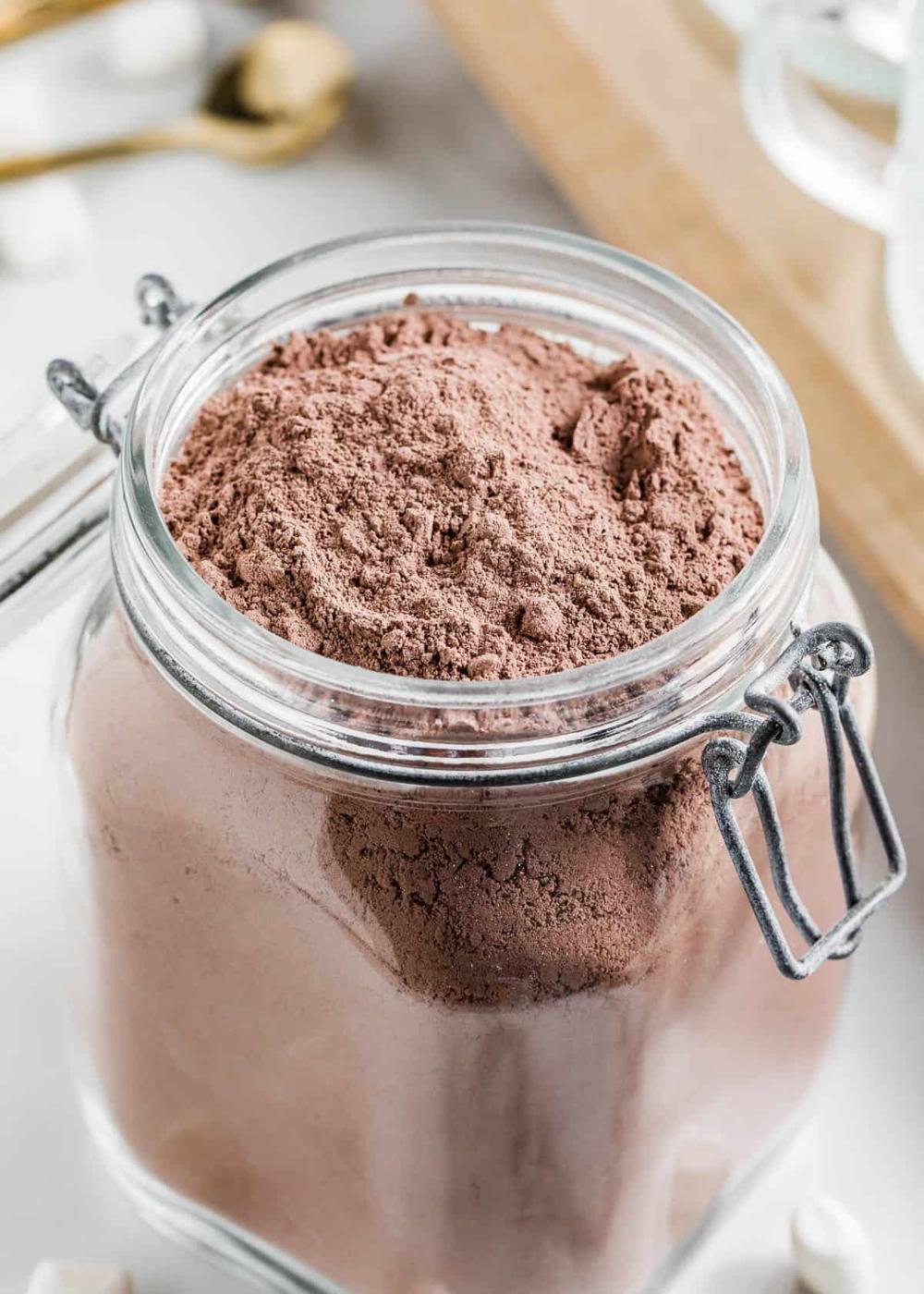 Glass clamp jar filled with dark cocoa powder mix on a pale counter with marshmallows blurred in the background