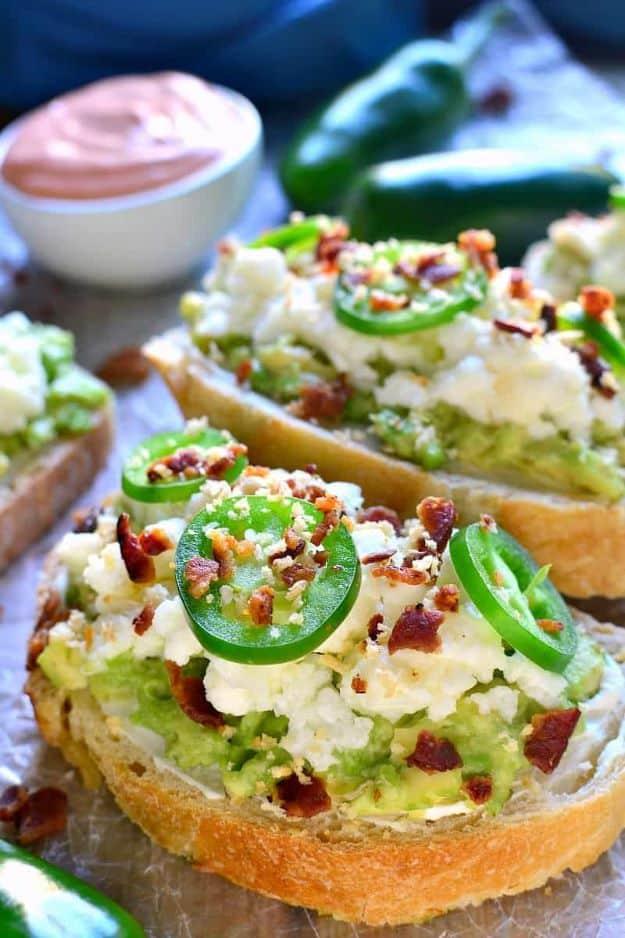 Jalapeno popper avocado toast, three slices topped with mashed avocado, cream cheese, jalapeno rings and bacon