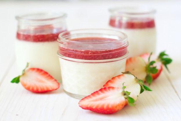 Strawberry panna cotta in small glass jars with a bright red berry layer on top and fresh berries beside them