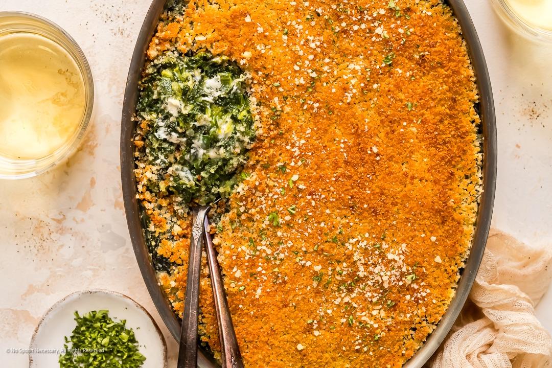 Creamy spinach bake under a golden panko and parmesan crumb, a spoon lifting it to show the green underneath