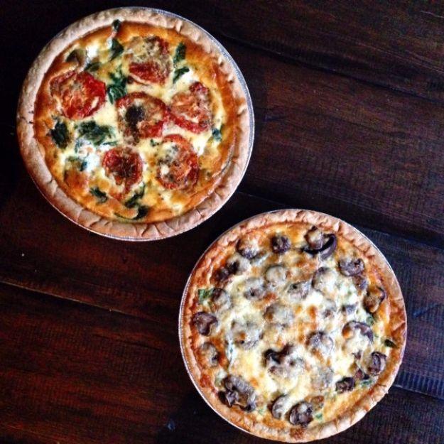 Two baked quiches overhead on dark wood, one with roasted tomato and spinach and one with black olives