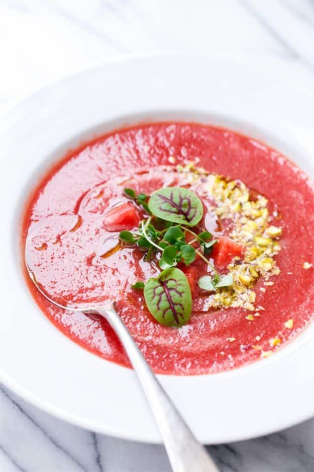 Tomato watermelon gazpacho in a white bowl topped with chopped pistachios, basil oil and fresh basil