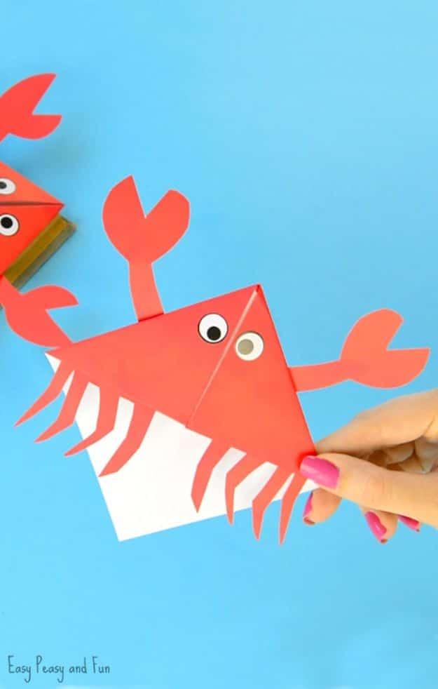 Red paper crab corner bookmark with cut claws and legs and googly eyes, held up on a bright blue background