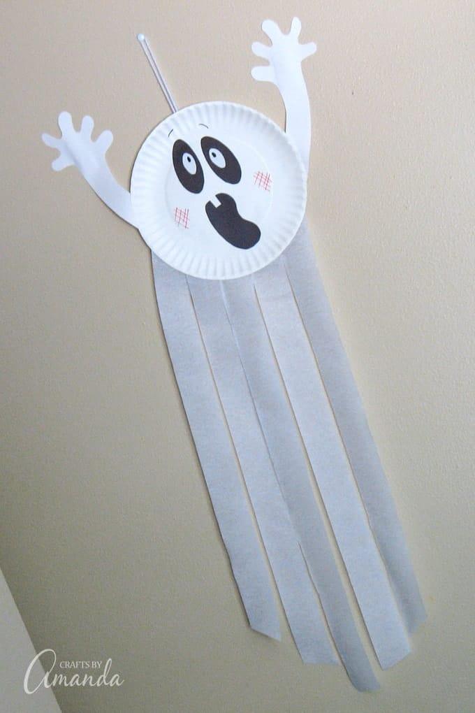 White paper plate ghost with construction-paper eyes and mouth, raised arms and five long white crepe-paper streamers
