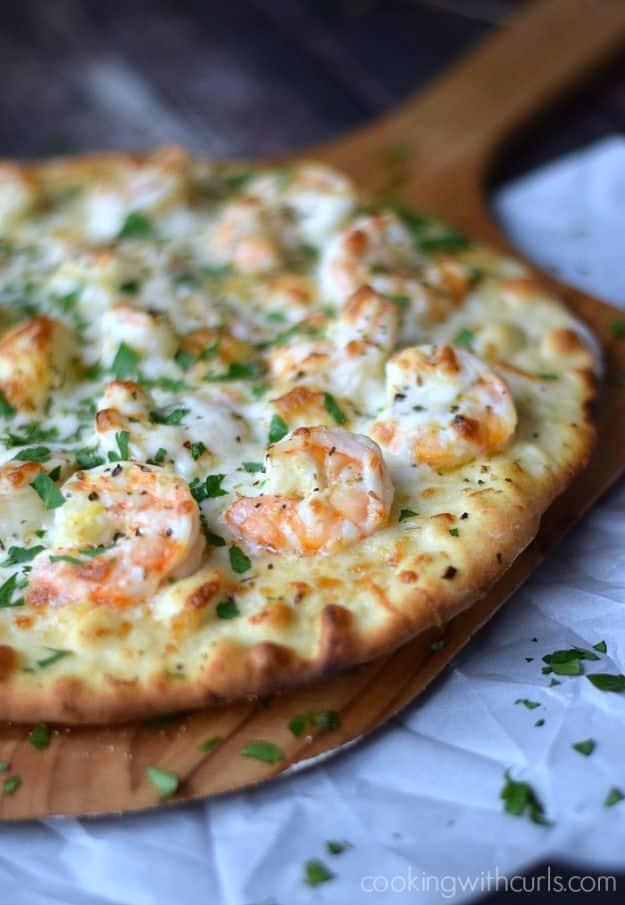 Shrimp scampi pizza on a wooden peel topped with whole shrimp, melted mozzarella and chopped parsley