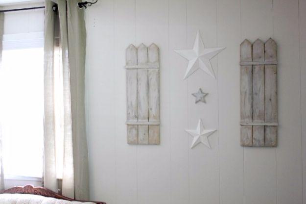Two weathered white picket shutters flanking a cluster of white stars on a pale board and batten bedroom wall
