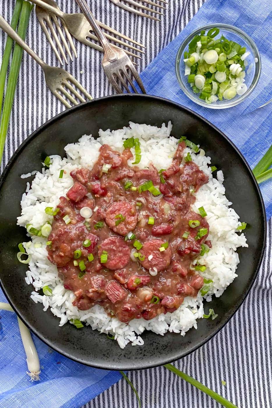 Red beans and rice in a bowl with sliced andouille sausage, diced ham and white rice, garnished with onion