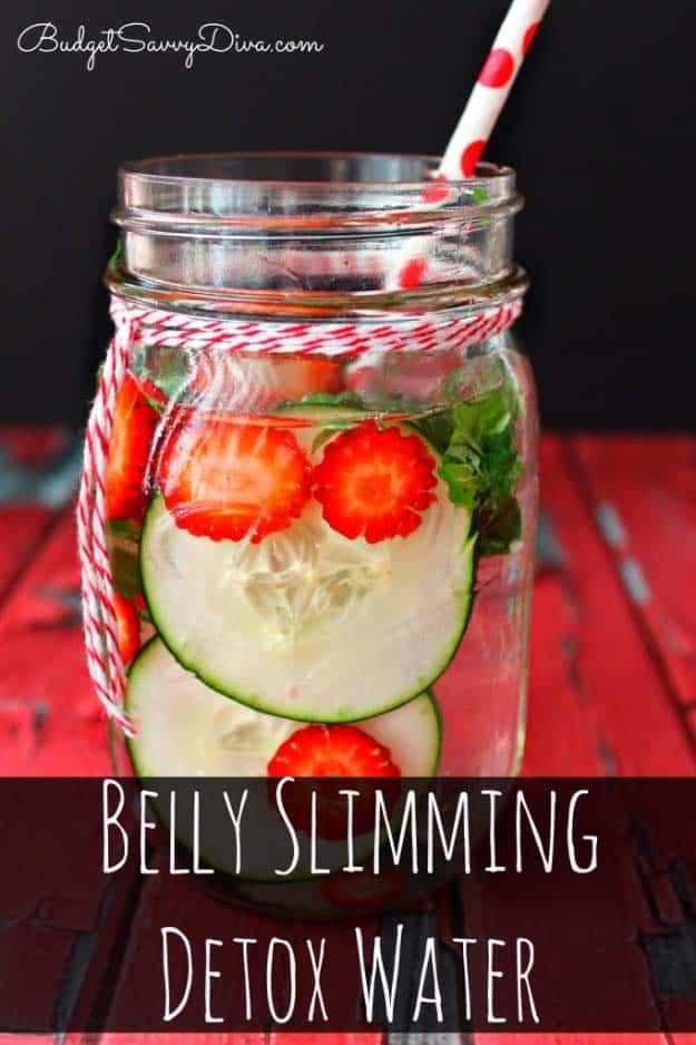 Belly slimming detox water in a mason jar with strawberry slices, cucumber rounds and a red striped straw