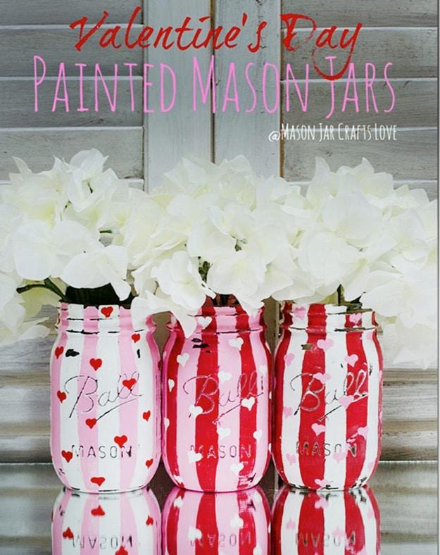 Chalk painted mason jars distressed back to bare glass in heart shapes, a farmhouse Valentine craft on a craft table