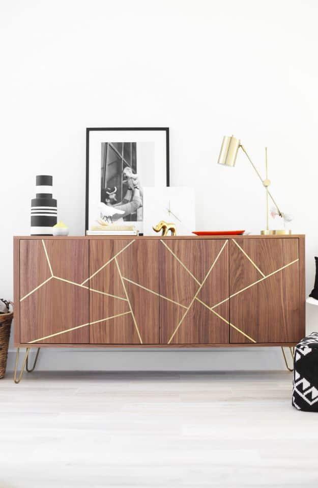 Walnut toned sideboard with a gold brass geometric inlay across four doors on gold hairpin legs, brass lamp and prints