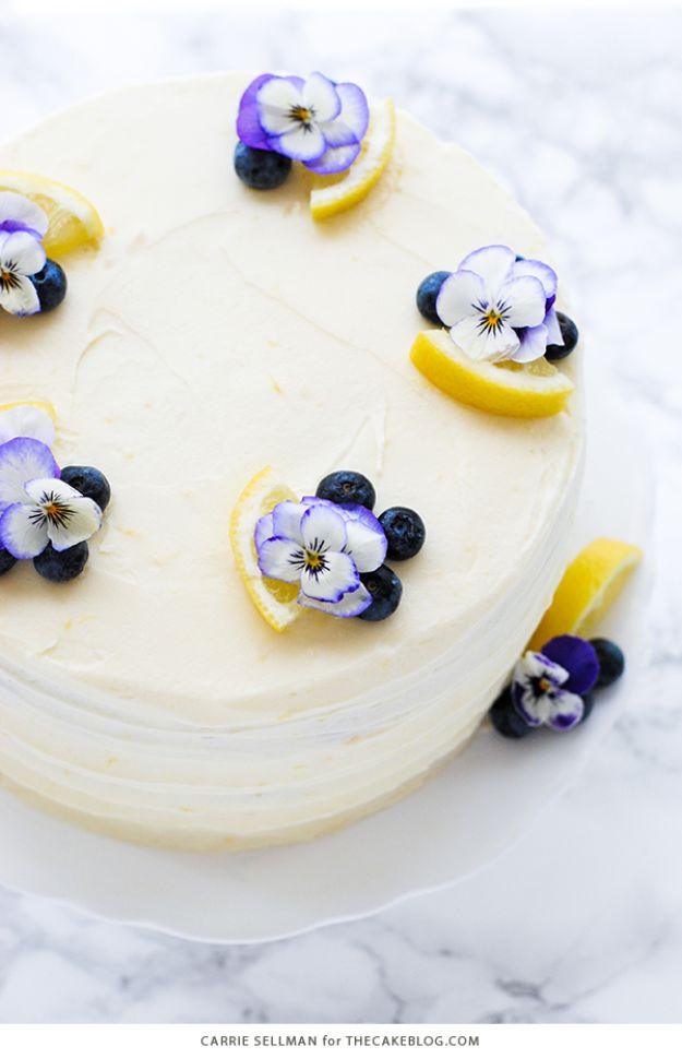 White frosted lemon blueberry cake topped with lemon slices, fresh blueberries and purple pansies on marble