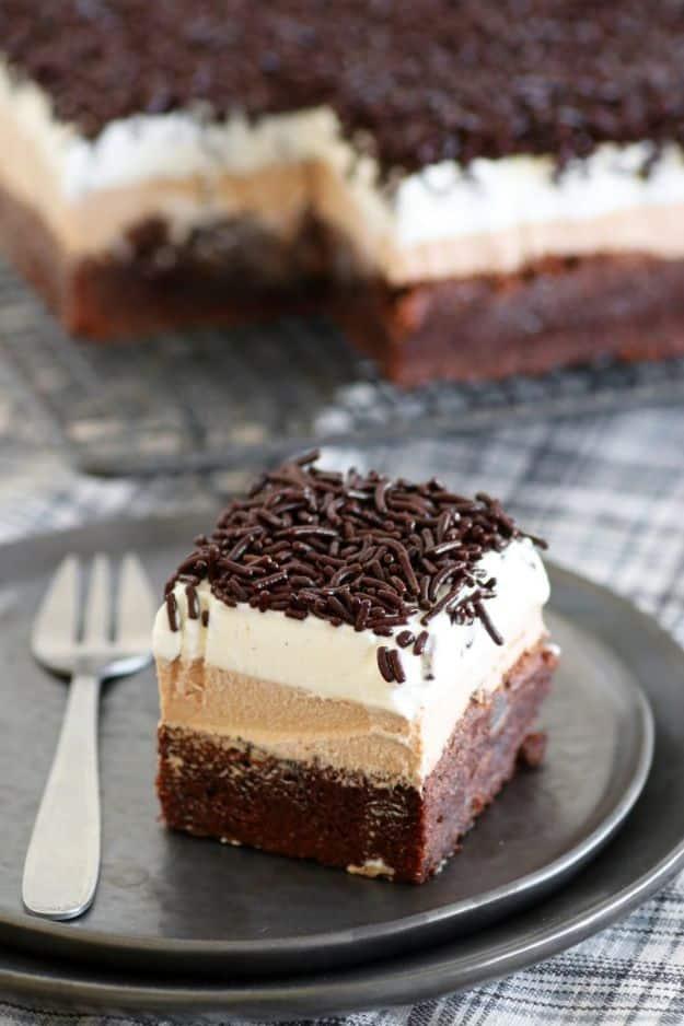 A slice of triple chocolate brownie cake with dark chocolate sprinkles on a grey metal plate with a fork
