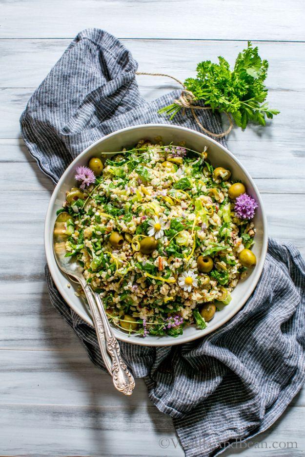 Spinach pecan brown rice salad in a wide shallow bowl with green olives and herbs beside a blue striped napkin