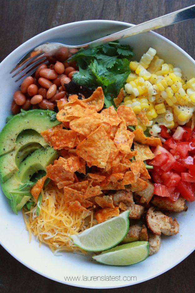 Southwest salad in a white bowl with crushed Doritos, sweet corn, pinto beans, sliced avocado, cheddar and lime wedges