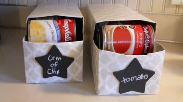 Two grey patterned fabric storage bins on a shelf holding soup cans, with black chalkboard star labels attached