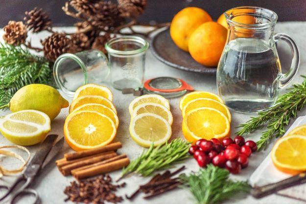 Sliced lemons and oranges, cinnamon, rosemary and cranberries laid out with glass jars and a pitcher of water