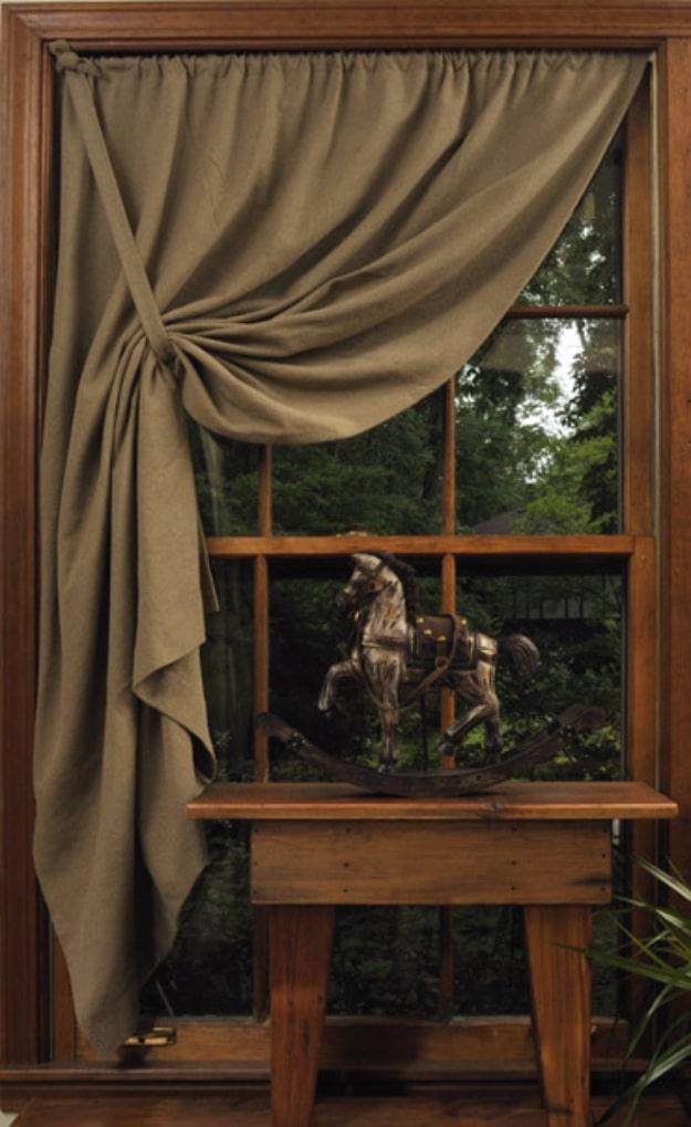 Taupe prairie cloth curtain pulled back to one side in a wooden window frame above a carved rocking horse
